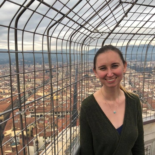 A picture of Amanda Woodward. She has brown hair in a pony tail. She is in Florence standing on top of the Duomo with Florence in the background