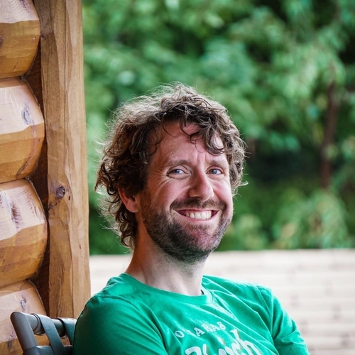 Logan Morrow smiles sitting outdoors at a cabin