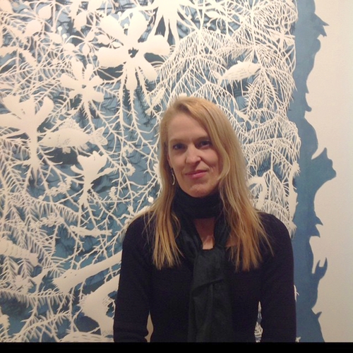 Sonja Peterson in front of her cut-paper artwork in white on blue wall