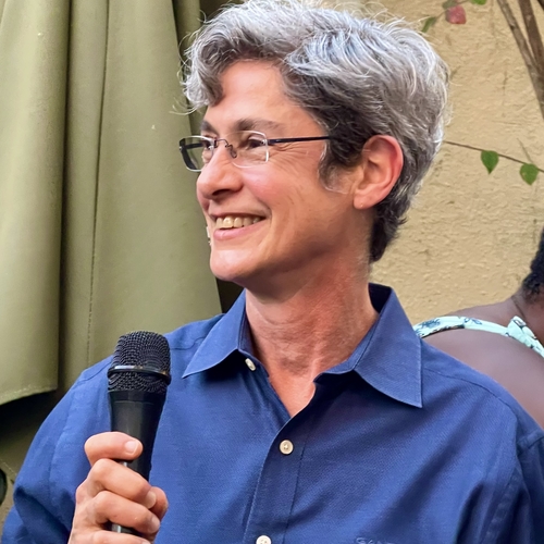 Photo of a smiling white lesbian with short gray hair, glasses, and a blue collared shirt.