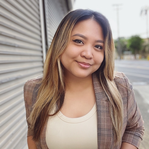 Blondish-brown hair Filipina woman sporting a white top and a brown blazer looking at the camera.
