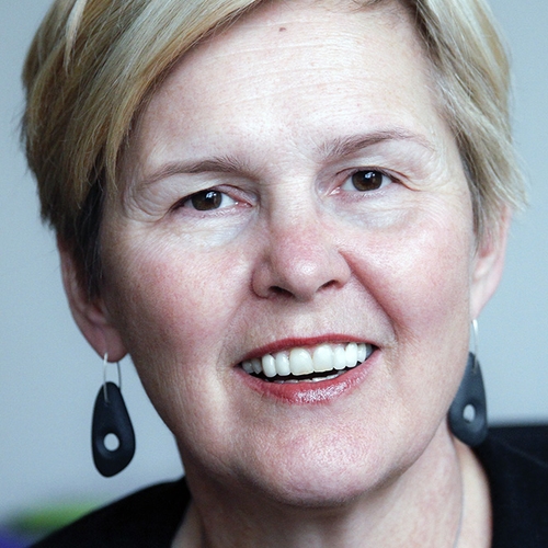 Caucaisan woman in her 60's, short blond hair, brown eyes, smiling, wearing a black shirt and black earings.