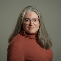portrait photo of woman in red turtleneck sweater with grey hair and glasses.