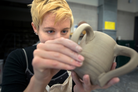 A student sculpts a ceramic mug in an arts studio. 