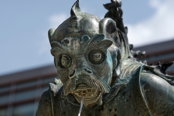 A gargoyle statue, close-up frame, spits water from its mouth into a fountain.