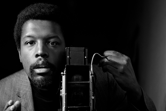 A Black man looks directly at an old fashioned 1960's camera snapping a self-portrait