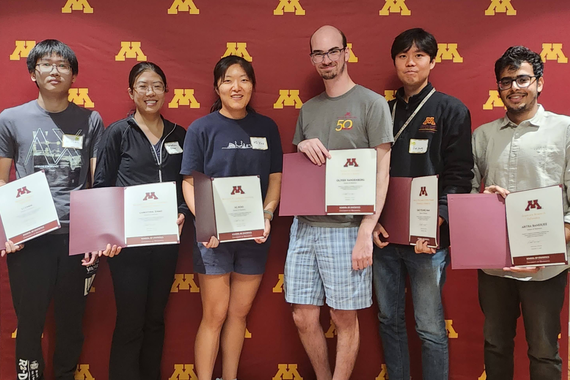 Students holding awards standing in front of a UMN backdrop