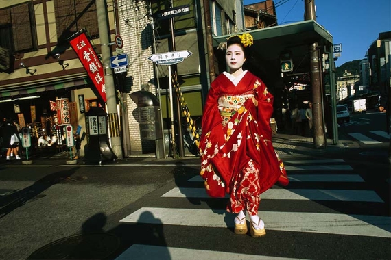 Kimono-clad geisha crosses a street in Kyoto, Japan during golden hour