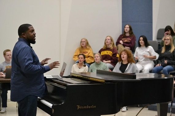 Adrian Davis standing in front of a piano and listening to his students singing 