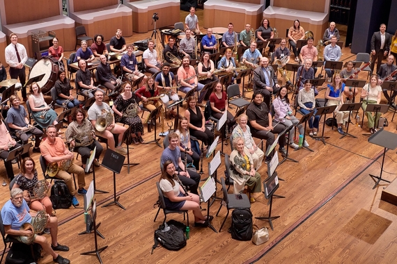 The afternoon workshop band of the Wind Band Conducting Workshop posing for a photo on the Ted Mann Concert Hall Stage