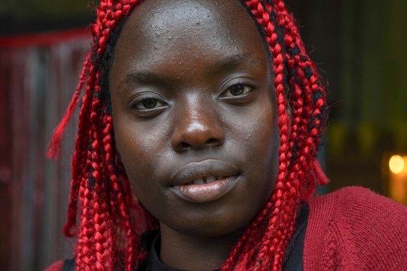 Photographic portrait of a young Black woman with bright red braids looks serenely at the camera as she tilts her head slightly to the side.