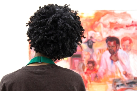 Back of a curly-headed student whose head is cocked as they look at a figurative painting.
