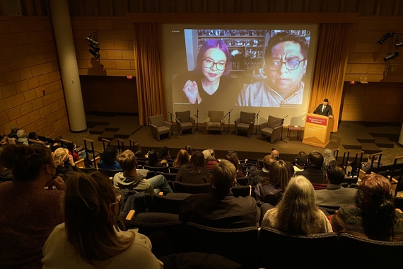 large group of people in an auditorium watching a video with two individuals