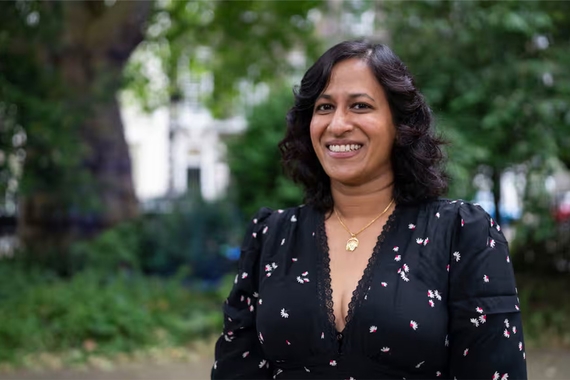 VV Ganeshananthan, a woman with brown skin and black hair, smiles in front of trees