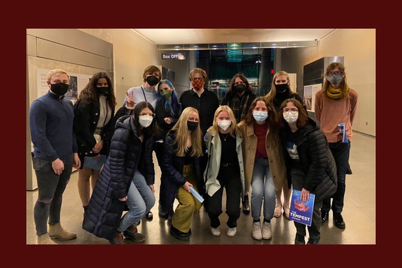 Maroon trim around photo of 13 people standing in hallway, five crouching down in front row, all wearing masks