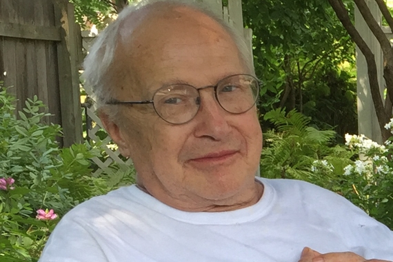 Smiling elderly white man sits in a garden wearing a white tshirt