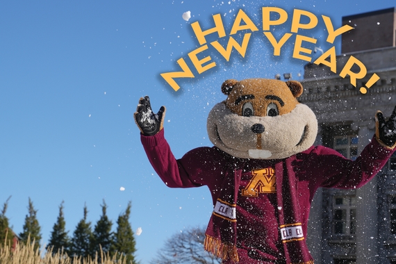 Goldy is wearing his CLA scarf, standing on the mall, and throwing snow and the words "Happy New Year"