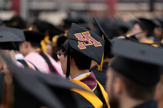 A graduate student picture shot from behind with the graduation cap as the focus. The UMN's logo sits right in the center.