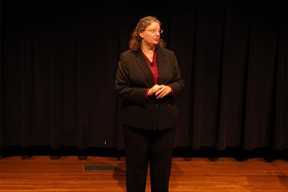 Rachel Croson, a white woman wearing a black blazer, stands on a stage