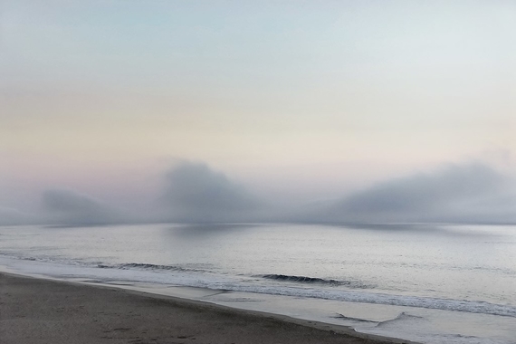 Marine fog rolls in Half Moon Bay, California. A section of sand can be seen. The horizon is blocked by fog.