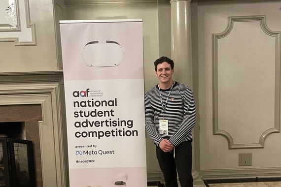Hamilton Peterson stands next to a pink banner that says "National Student Advertising Competition"