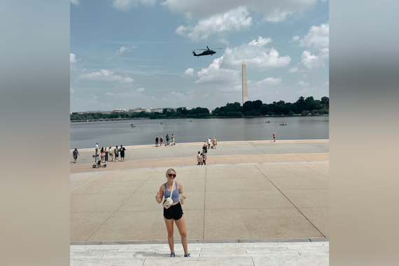 Isabella standing in front of body of water with helicopter and Washington Monument in background.