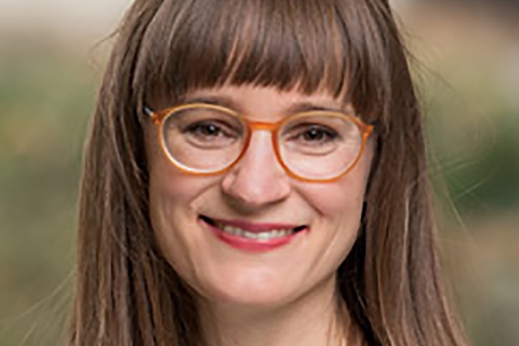 Associate Professor Janette Dill, a person with long, brown hair and light skin wearing glasses and smiling, wearing a grey sweater