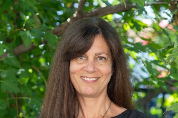 A photo of a person with dark hair wearing a black shirt standing in front of a tree