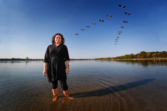 Image of Kate Beane standing in a lake with a V formation of birds in the sky above her