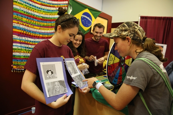 Woman wearing a hat looks at images on a paper held up by a woman in a t-shirt. A man and woman in the background watch and smile.