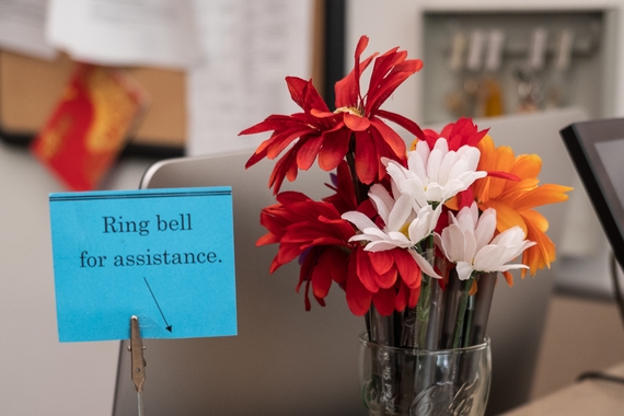 A "ring bell for assistance" sign is displayed on an office desk, along with a container of flower pens.