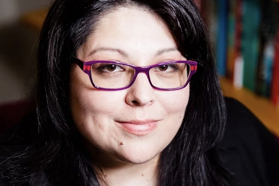 Photo of head of person with dark hair to shoulders, pink-red glasses, light skin