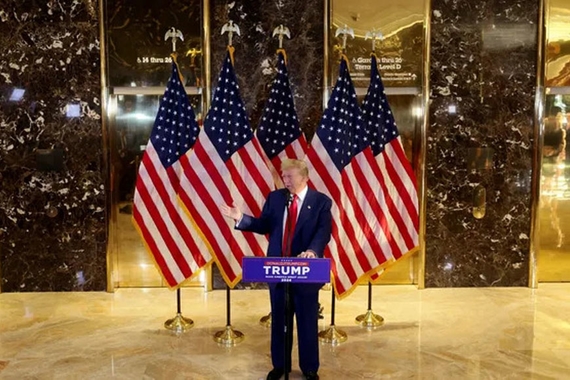 Donald Trump speaks at podium in front of five American flags