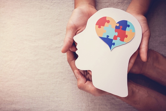 Stock image of two pairs of hands holding a cutout of a head, with a heart made of puzzle pieces over the top of the head