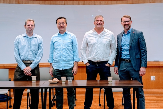 Jeff Lande, Xiaoyi Zhu, Paul Boruta, Nathan Hubbell. Standing in a classroom. Pannel