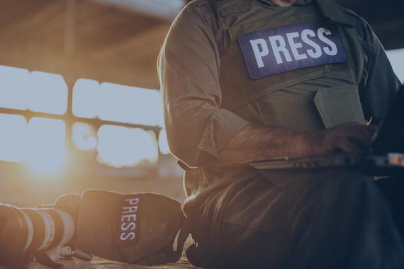 Press worker sits in a warehouse wearing a 'Press' vest next to a camera