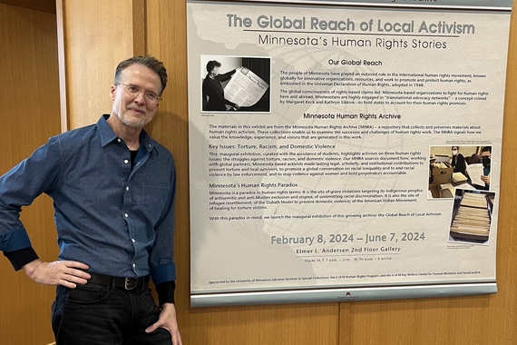 "Global Reach of Local Activism" archival exhibit designer, Darren Terpstra, standing next to the introductory panel of the exhibit
