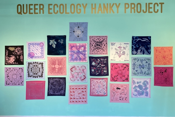 An aqua wall with colorful bandanas depicting a range of ecological and sexual imagery. "Queer Ecology Hanky Project" is in gold text on top.