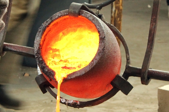 Molten metal glowing yellow is poured out of a large red-hot cup