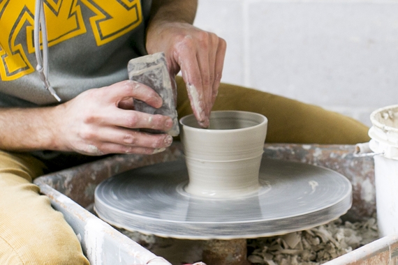 A student in a UMN sweatshirt forms a clay vessel on a potter's wheel