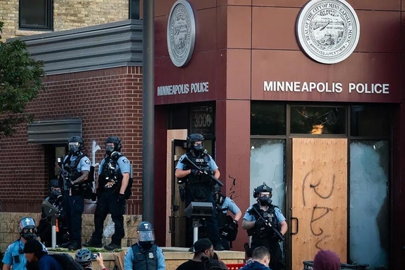 Minneapolis police in riot gear stand in front of shuttered Minneapolis police department building