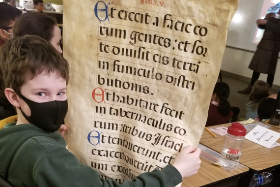 A 4th grade student holds up an large manuscript page