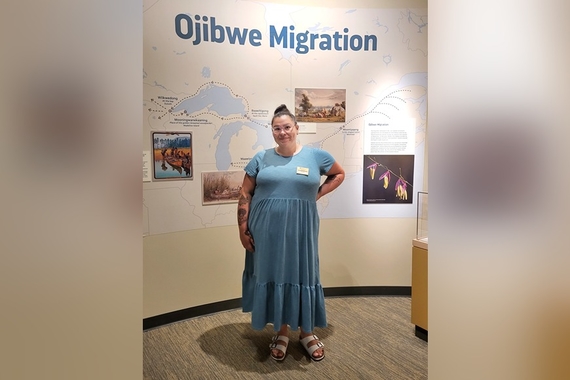Selena Bernier in front of an exhibit labeled "Ojibwe Migration"
