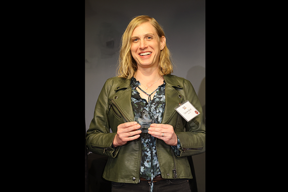 Carrie Strief holds her Alumni Award, appearing from the waist up against a plain grey backdrop.