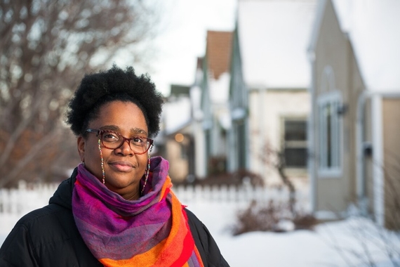 Taiyon J. Coleman photographed before a line of snow-coated houses.
