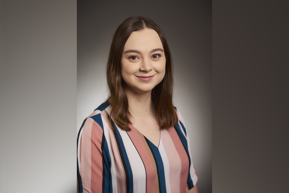 Briana Beeman, a young woman in a striped shirt, smiles in front of a gray background