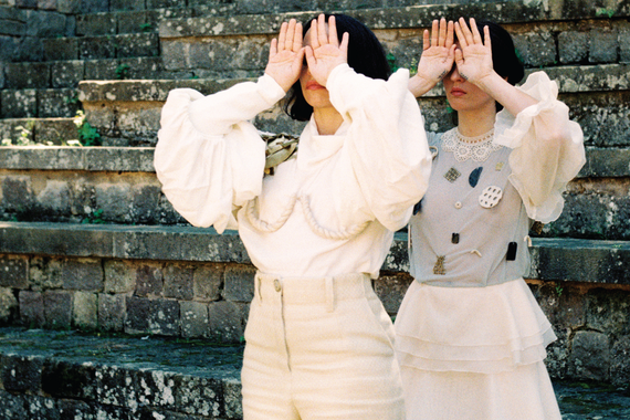 photograph of two women in cream outfits with their hands over their eyes