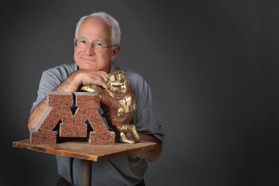 Man with glasses and gray hair smiling with a model of the University of Minnesota "M" and Goldy Gopher