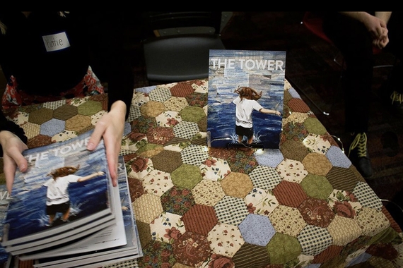 Patchwork quilt over table with hands on stack of magazines to left and magazine propped on table to right; magazine cover shows person jumping into water and text The Tower