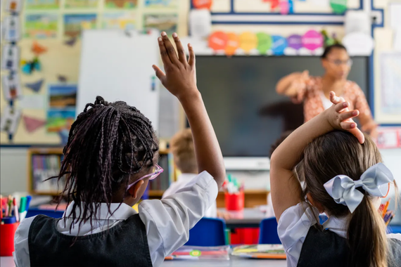 Two young elementary students raising their hands in a classroom setting